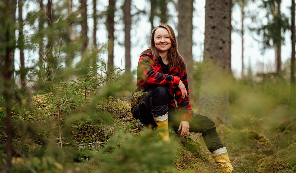 Anne-Mari Tarkkio sitter på en mosstuva i sin egen skog. 