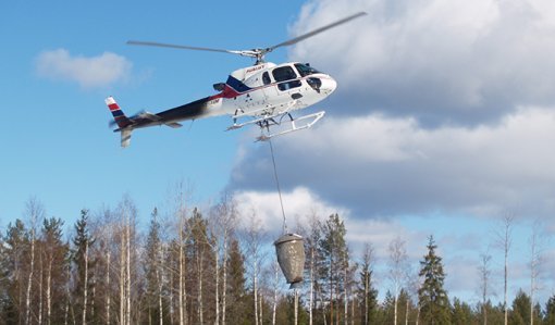 Helikoptern sprider ut askgödselmedel i skogen. 